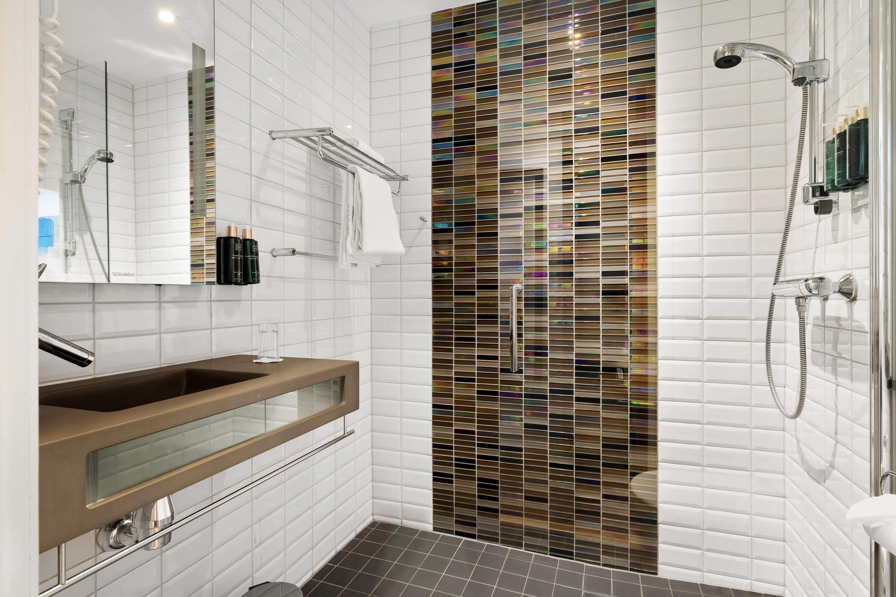 A modern bathroom with a glass shower enclosure, a vanity with a mirror, and a tiled floor.