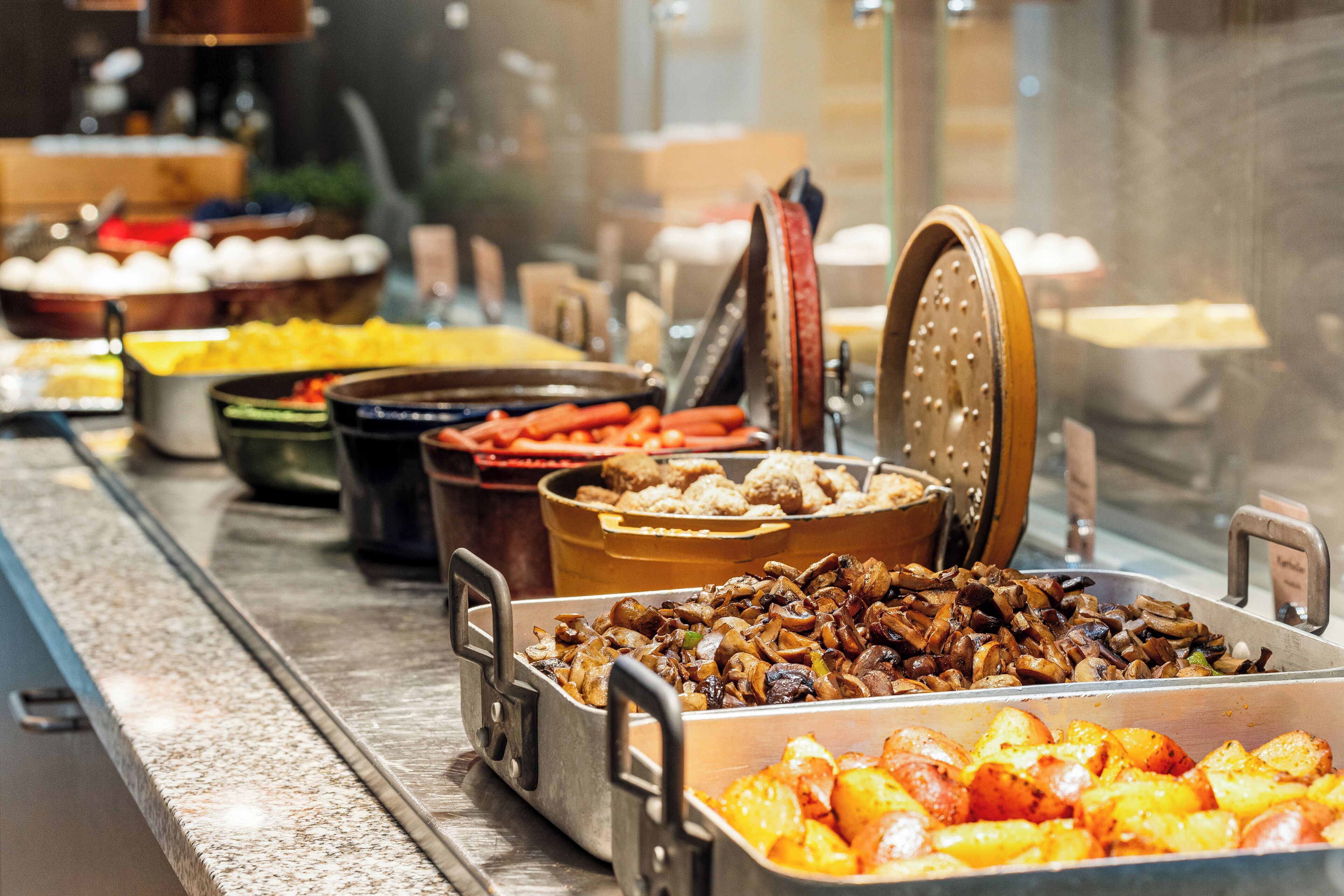 A buffet with various dishes including roasted potatoes, mushrooms, and other prepared foods.