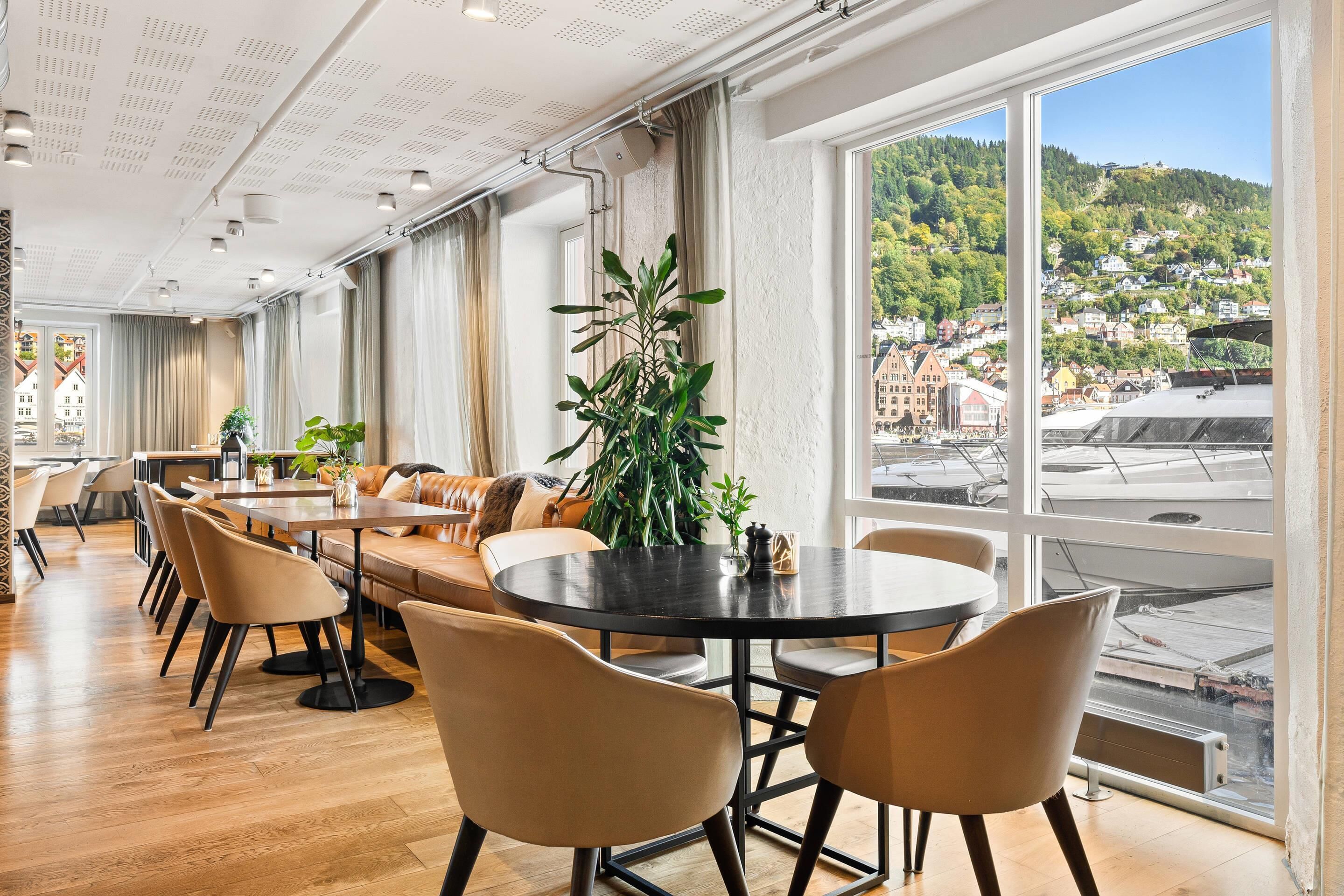 A modern dining area with a round table and chairs, large windows with a city view, and a plant centerpiece.