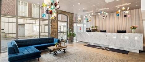 A modern hotel lobby with a blue sofa, a marble reception desk, and a large window offering a view of the street.