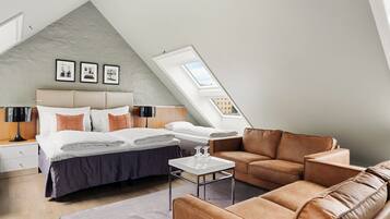 A modern bedroom with a sloped ceiling, a bed, a sofa, and a small table.