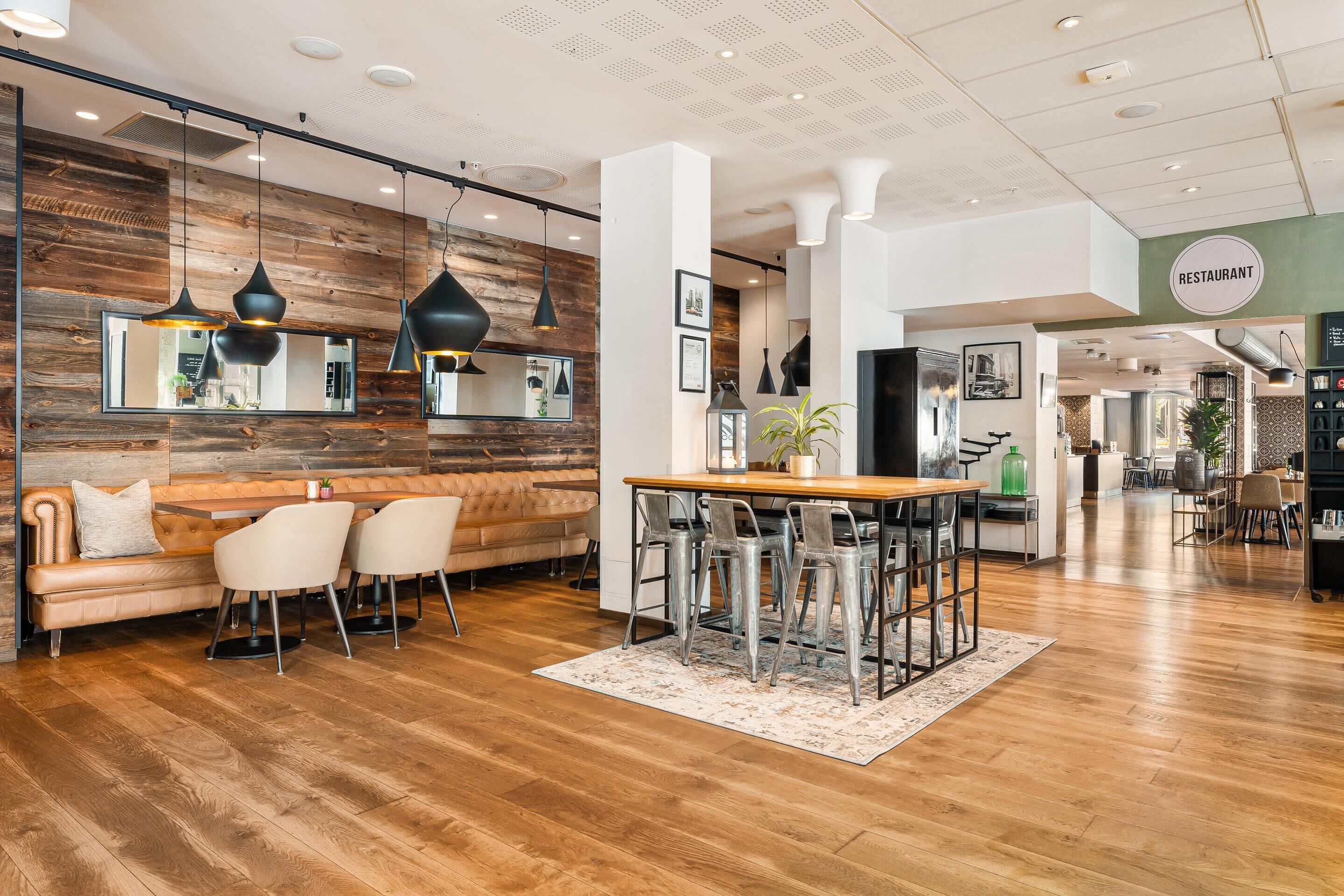 A modern restaurant interior with a wooden accent wall, a dining area with a wooden table and metal chairs, and a bar area with stools.