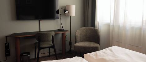 Ein Hotelzimmer mit Bett, Schreibtisch, Stuhl, Fernseher und Lampe.