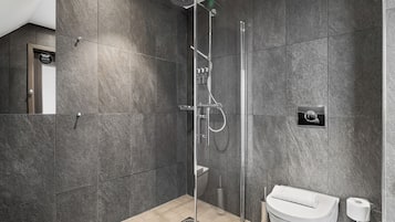 Un baño moderno con ducha envuelta en vidrio, inodoro y dispensador de toallas.
