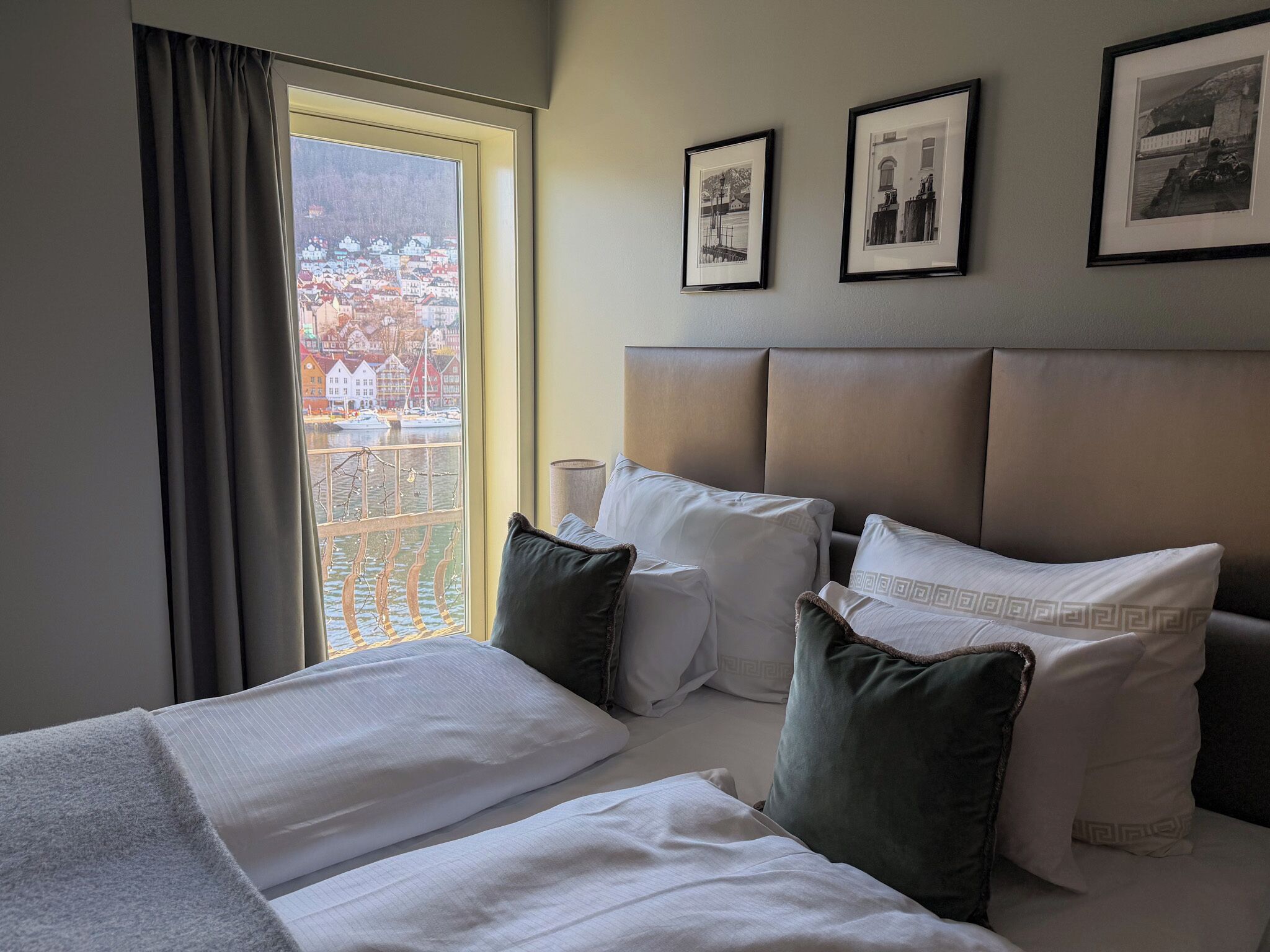 A hotel room with a bed, a window with curtains, a headboard, and three framed pictures on the wall.
