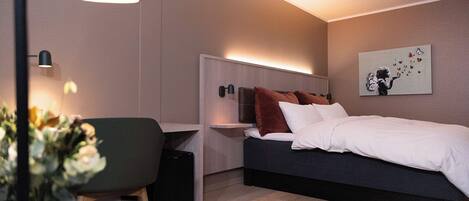 A modern bedroom with a bed, bedside tables, a desk, and a chair.