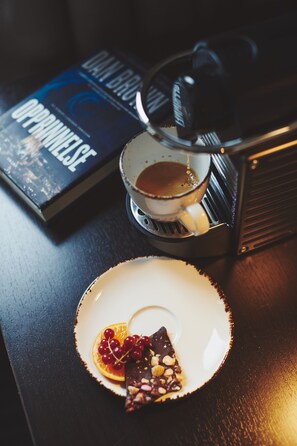 A coffee machine, a book titled "Opponelse," and a plate with chocolate and fruit on a wooden table. - Stord Hotell (Stord)