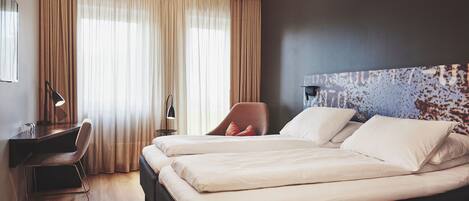 A hotel room with two beds, a desk, a chair, and a large window with curtains.