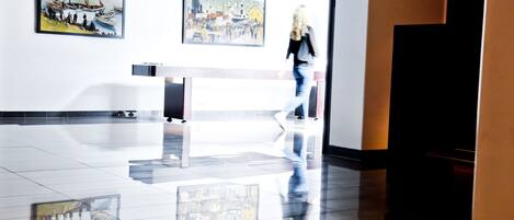 A spacious lobby with a polished floor reflecting artwork and a woman walking.