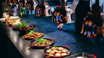 A buffet setup with various dishes in pans and bowls, a person in the background, and hanging lights.