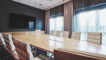 A conference room with a long table, six chairs, a large screen, and large windows with curtains.