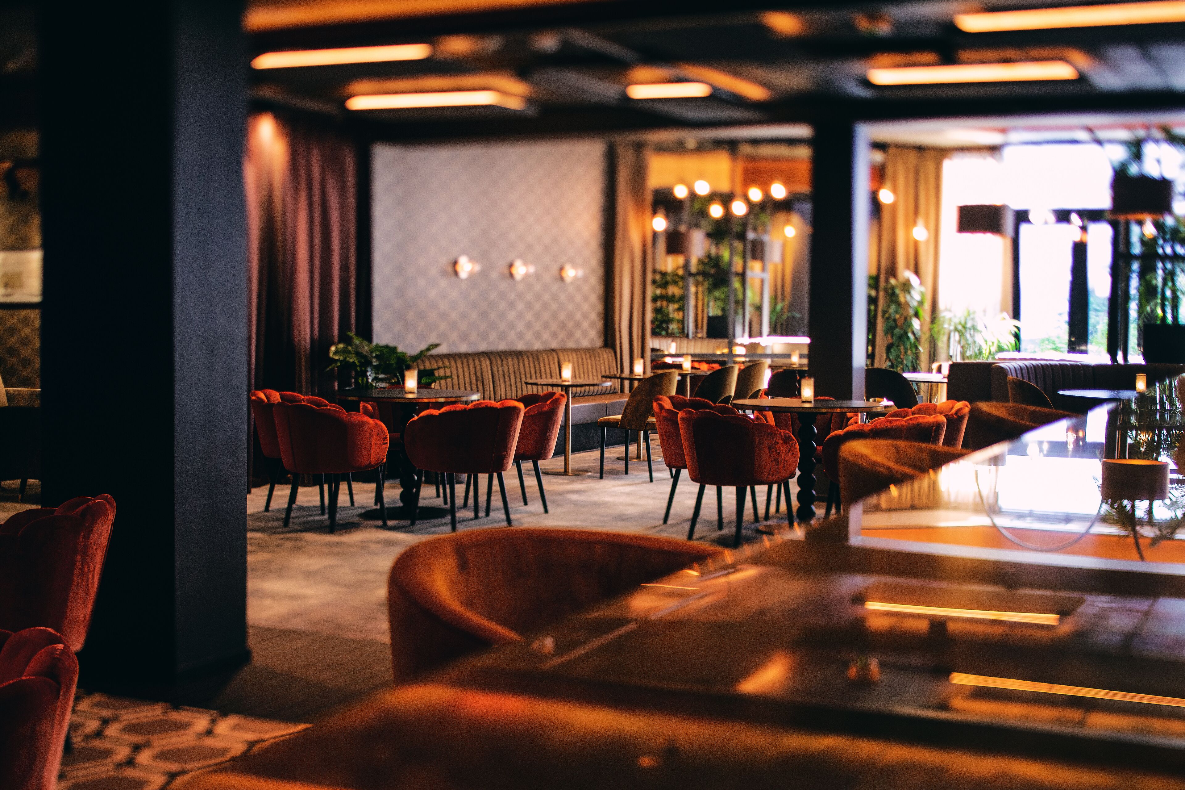 Un intérieur de restaurant moderne avec des chaises à revêtement rouge, un bar et un éclairage d’ambiance.