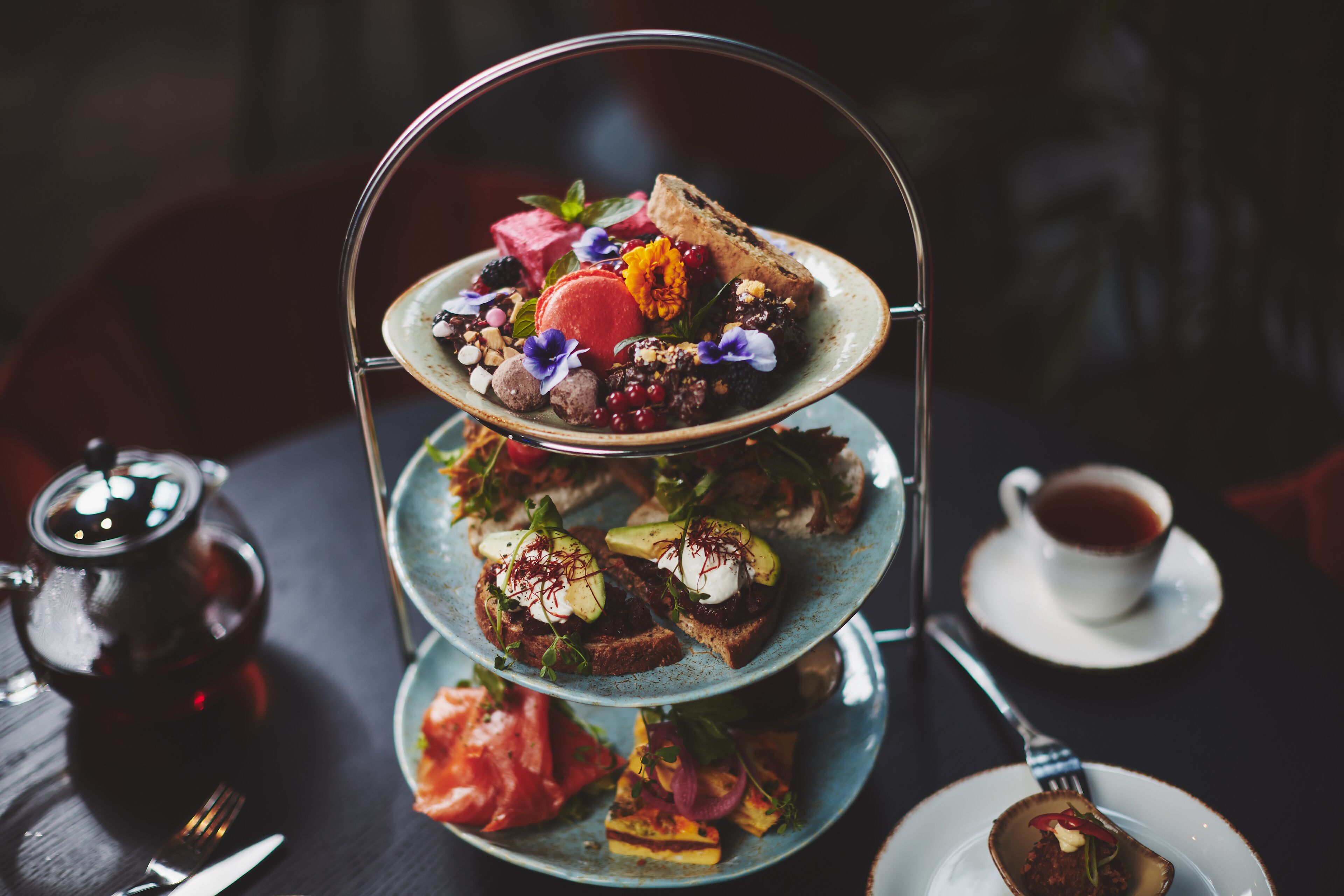 Un frutero escalonado con varios pasteles y una taza de té sobre una mesa.