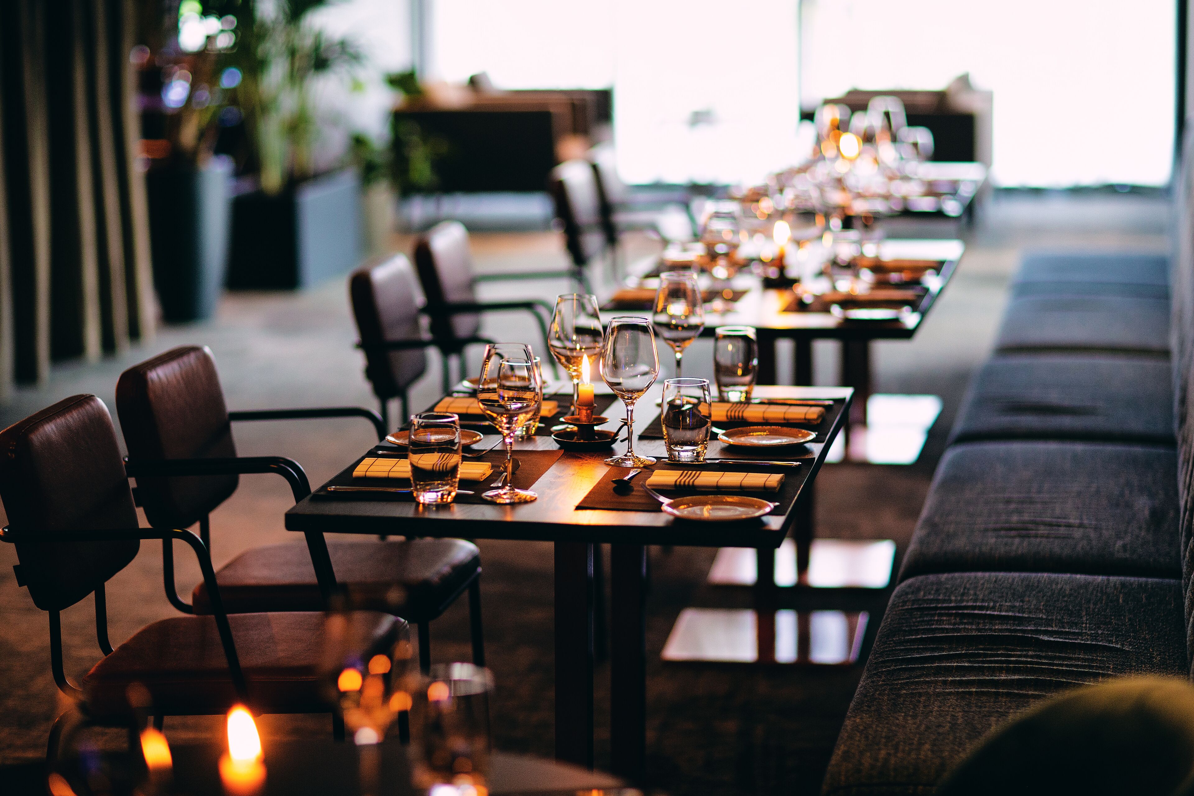 A restaurant with long tables set for dining, chairs, and candles.