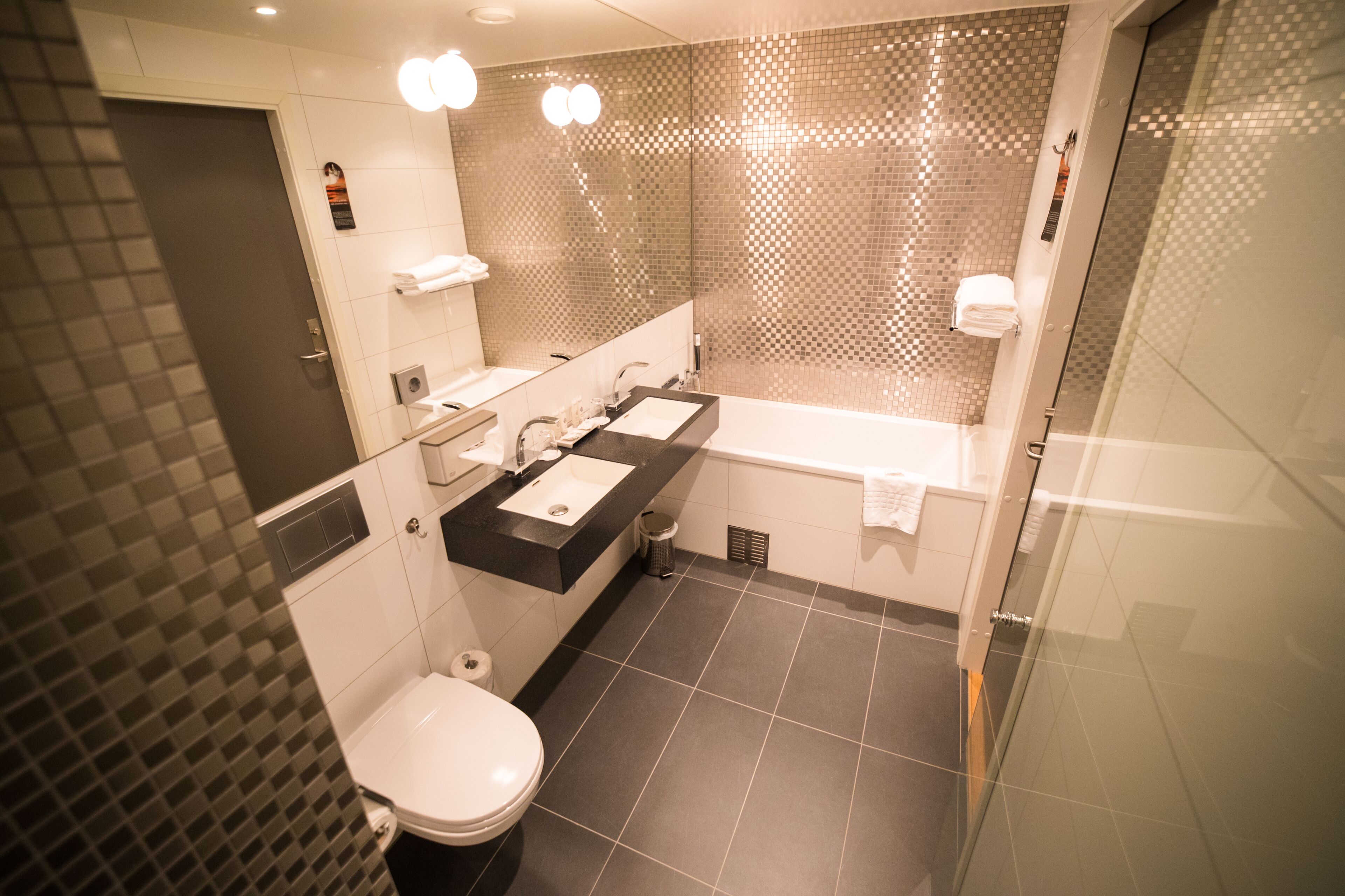 A modern bathroom with a toilet, two sinks, a bathtub, and a shower area.