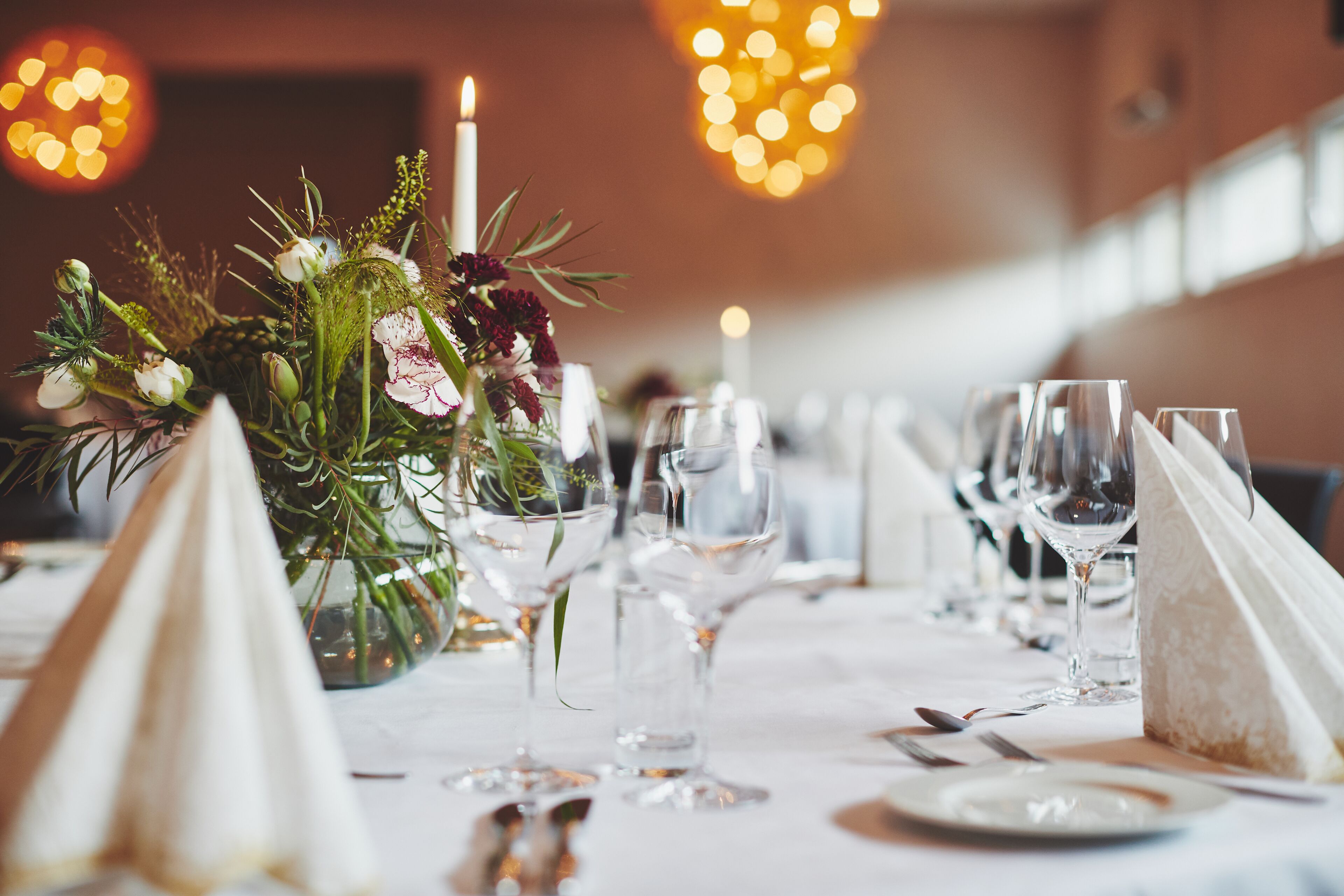 A table set for a formal dinner with a centerpiece of flowers and candles, glasses, and cutlery.