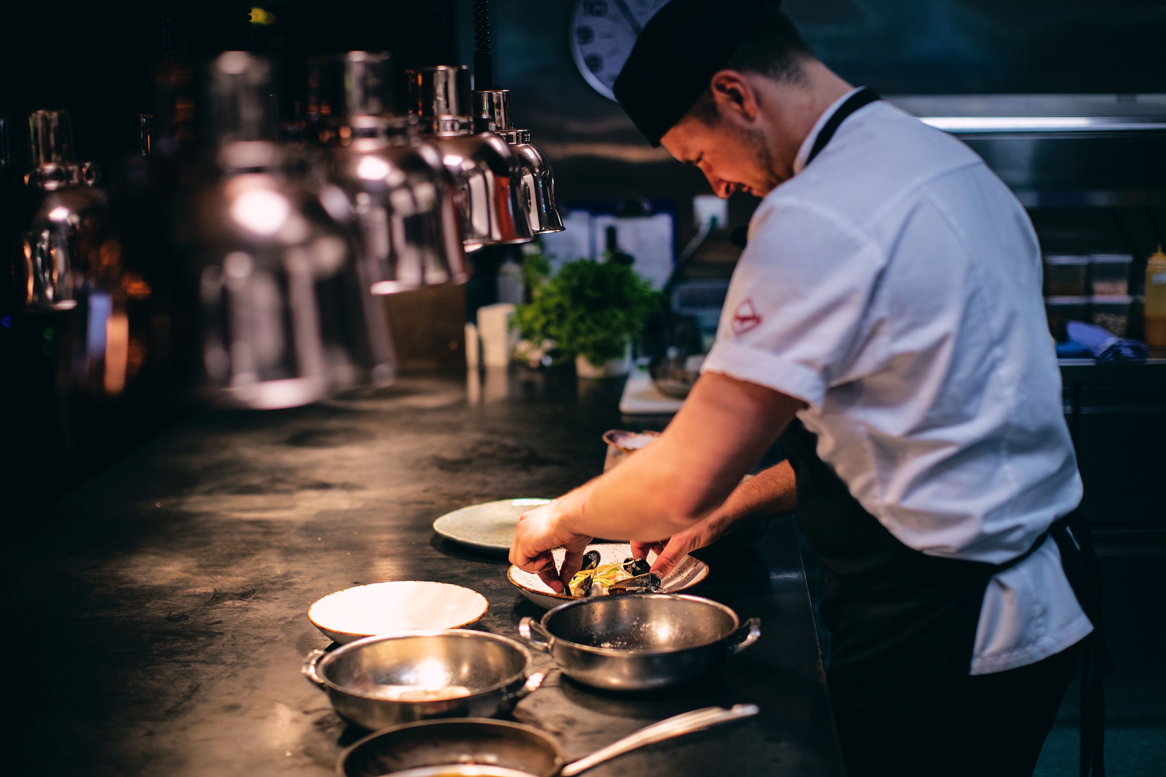 Un chef preparando comida en una cocina profesional con equipo de acero inoxidable y un espacio de trabajo limpio y ordenado.