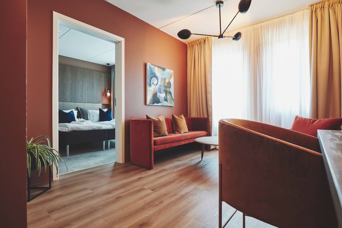 Un salon moderne avec un plancher en bois, un canapé rouge, une petite table et un tableau accroché au mur.