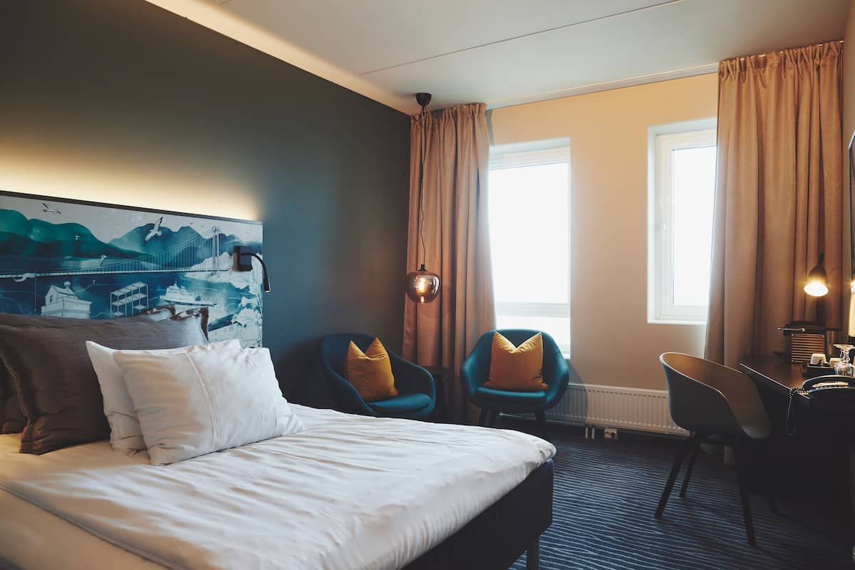 Une chambre d’hôtel avec un lit, deux chaises, un bureau et une fenêtre avec des rideaux.