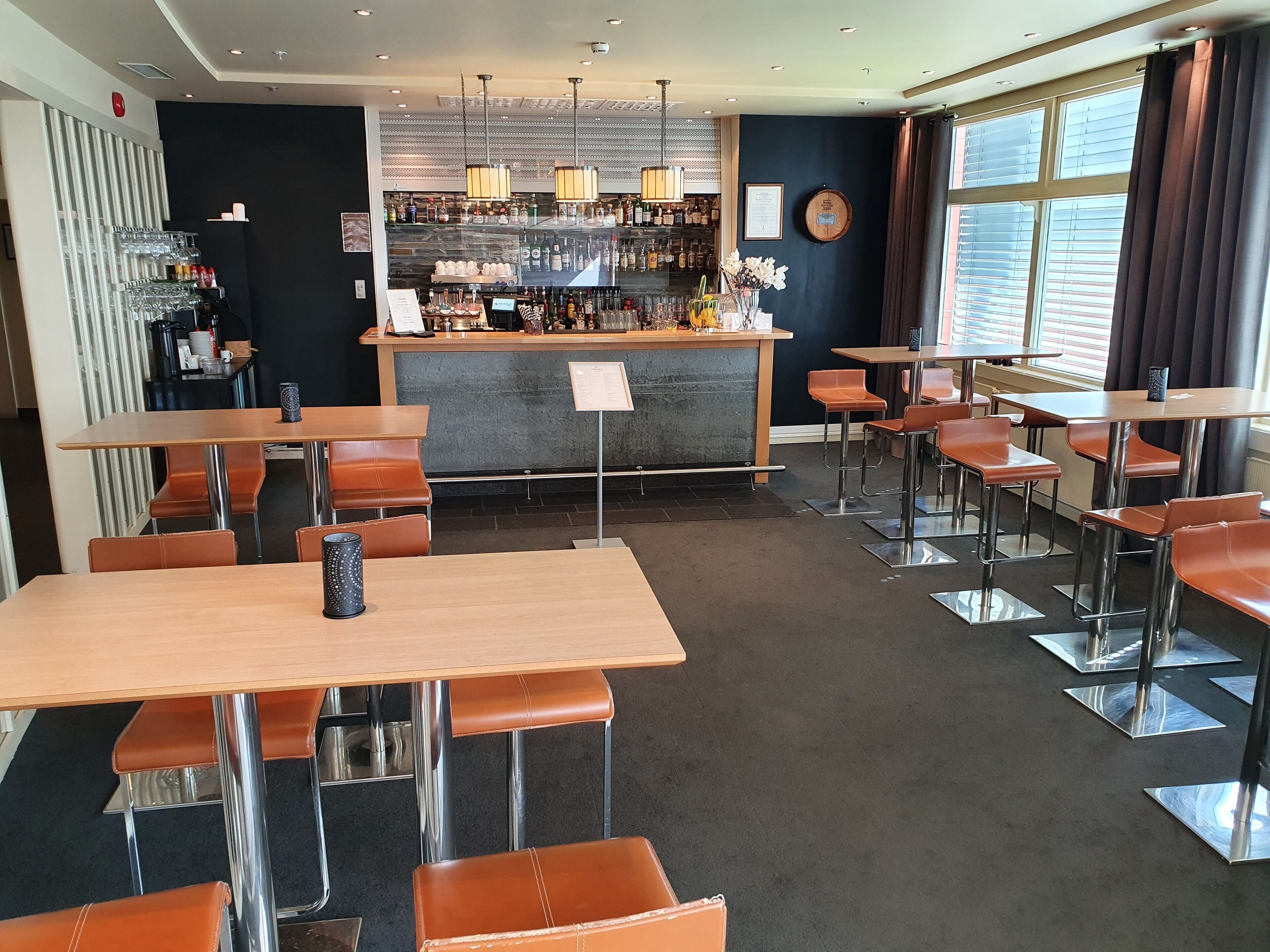 A restaurant with multiple tables and booths, a bar area with various bottles, and a large window with curtains.