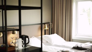 A hotel room with a bed, a bedside table with a lamp, a coffee maker, and a window with curtains. - Roros Hotell (Roros)
