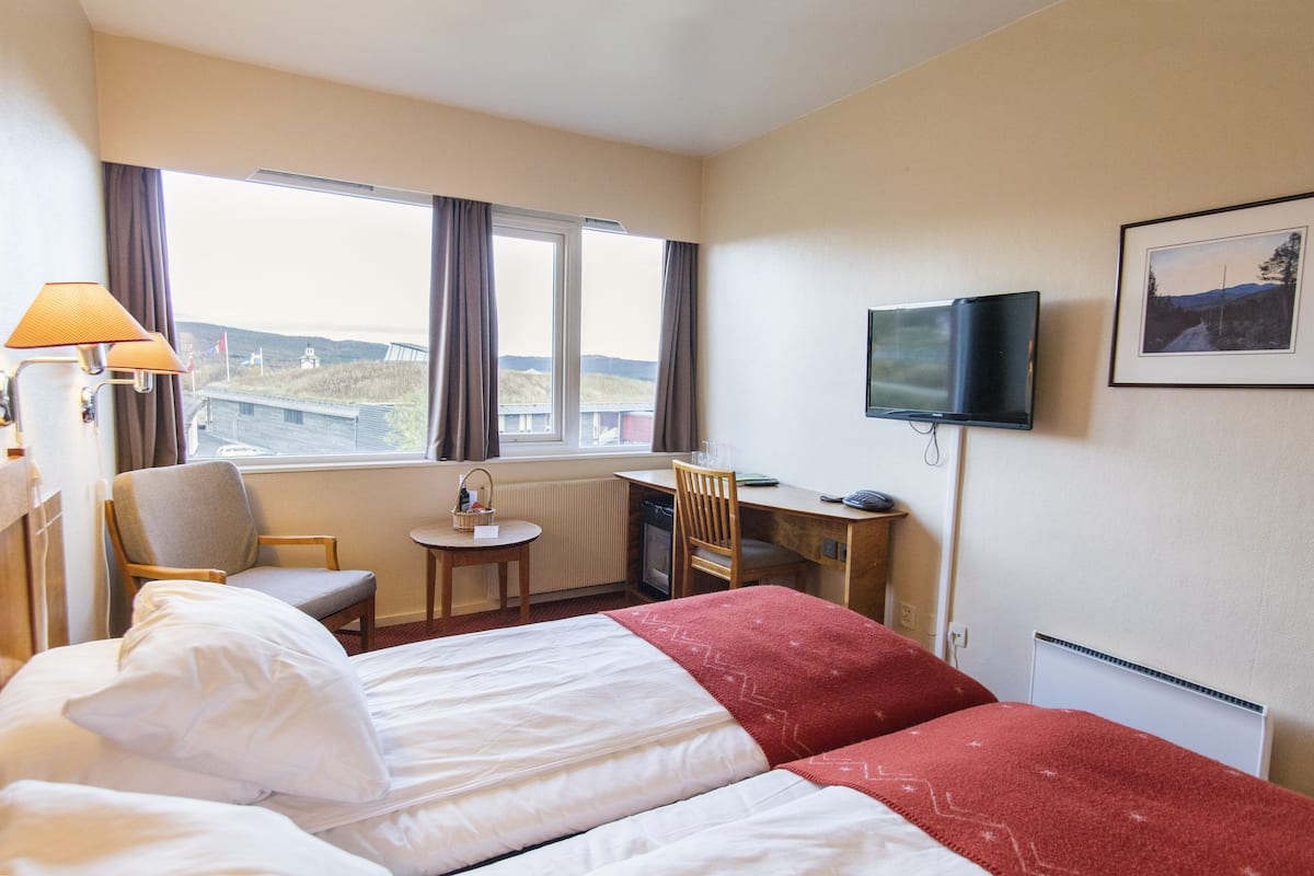 Ein Hotelzimmer mit Bett, Schreibtisch, Stuhl, Fernseher und Fenster mit Aussicht.