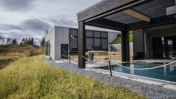 A modern building with a pool area, featuring a wooden deck and a covered seating area. - Roros Hotell (Roros)