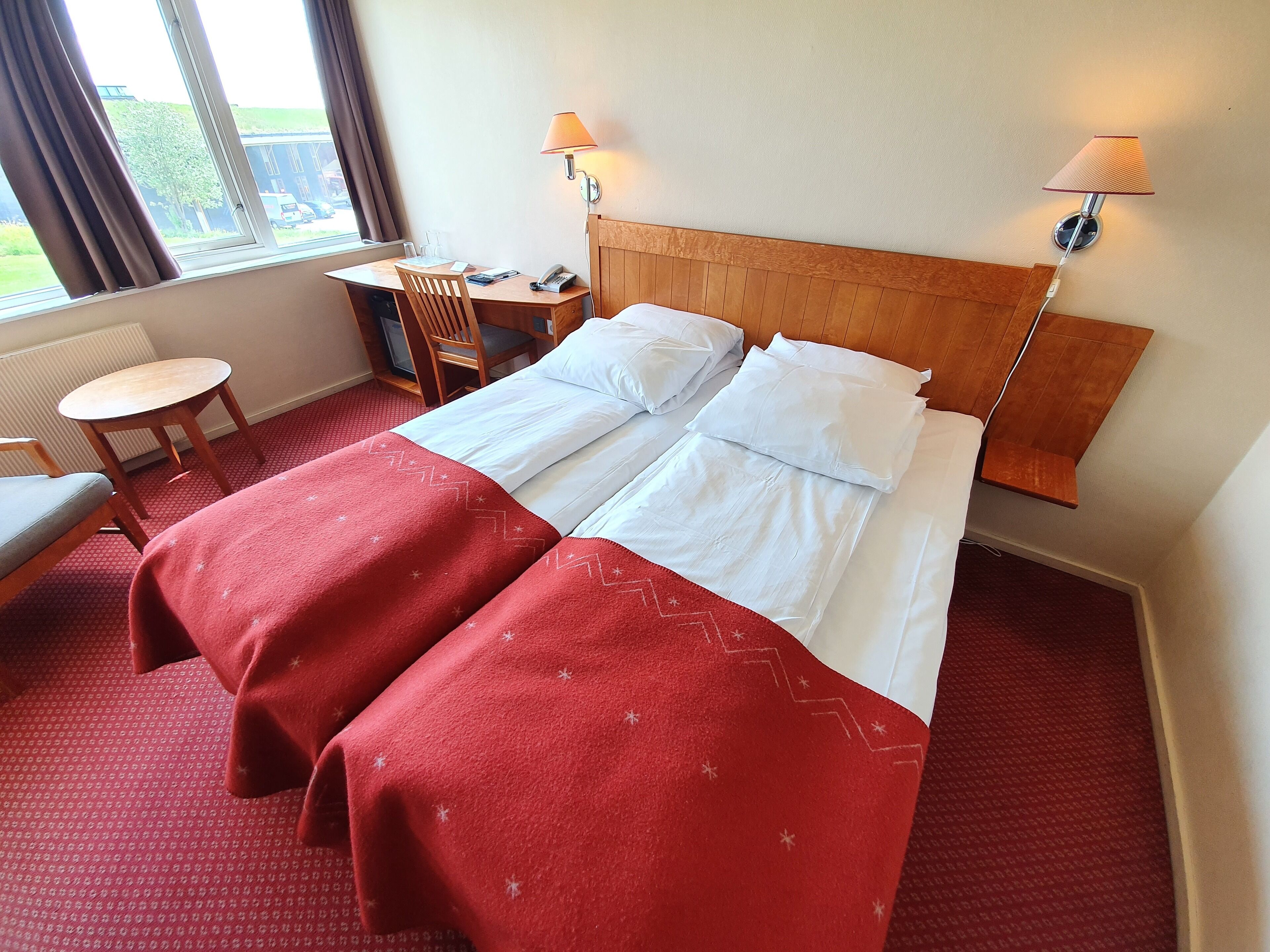 A hotel room with two beds, a desk, a chair, and two bedside lamps.