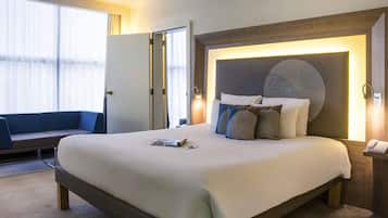Ein Hotelzimmer mit einem großen Bett, einem Nachttisch mit Telefon, einer Wandleuchte und einer Sitzecke mit Sofa und Vorhängen.