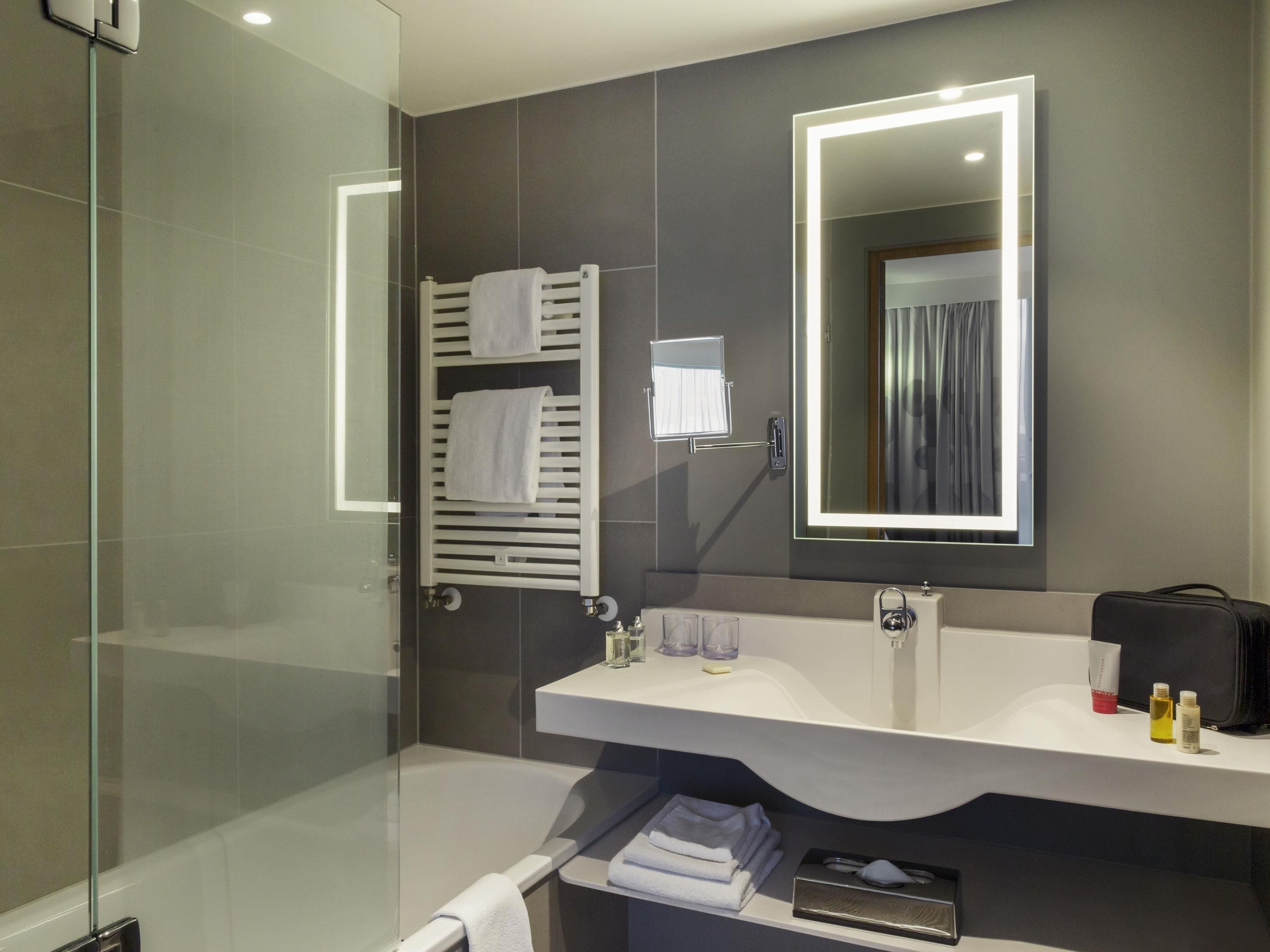 Un baño moderno con cabina de ducha de vidrio, tocador blanco con espejo y un perchero para toallas.