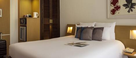 A hotel room with a large bed, bedside tables, a wardrobe, a desk, and a painting on the wall.