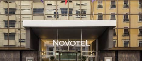 A hotel entrance with a glass facade, a sign reading 'Novotel,' and a revolving door.