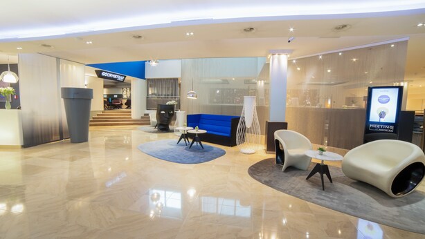 A modern lobby with a blue sofa, white armchairs, and a reception desk. - Novotel Geneve Centre (Geneva)