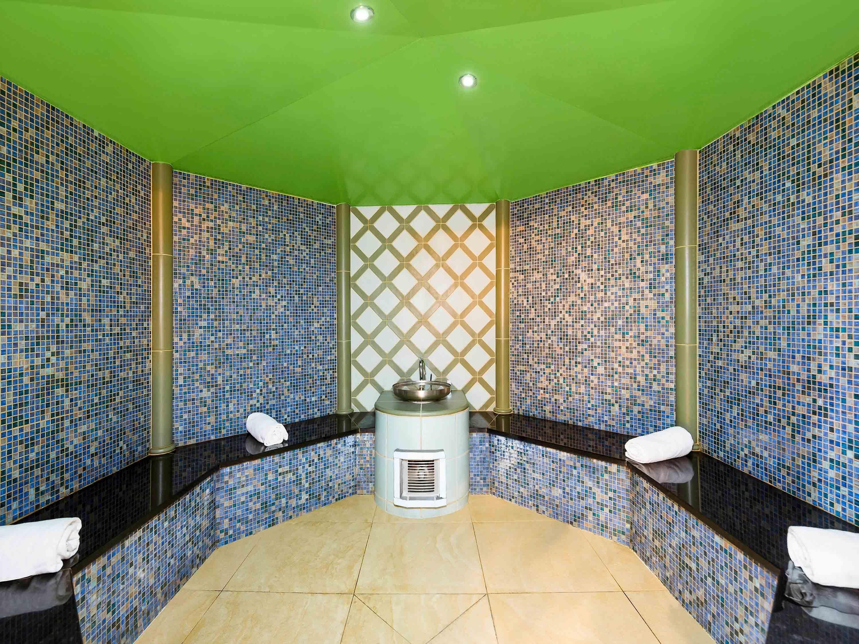 A spa room with mosaic tile walls, a central heating unit, and two white towels on the floor.
