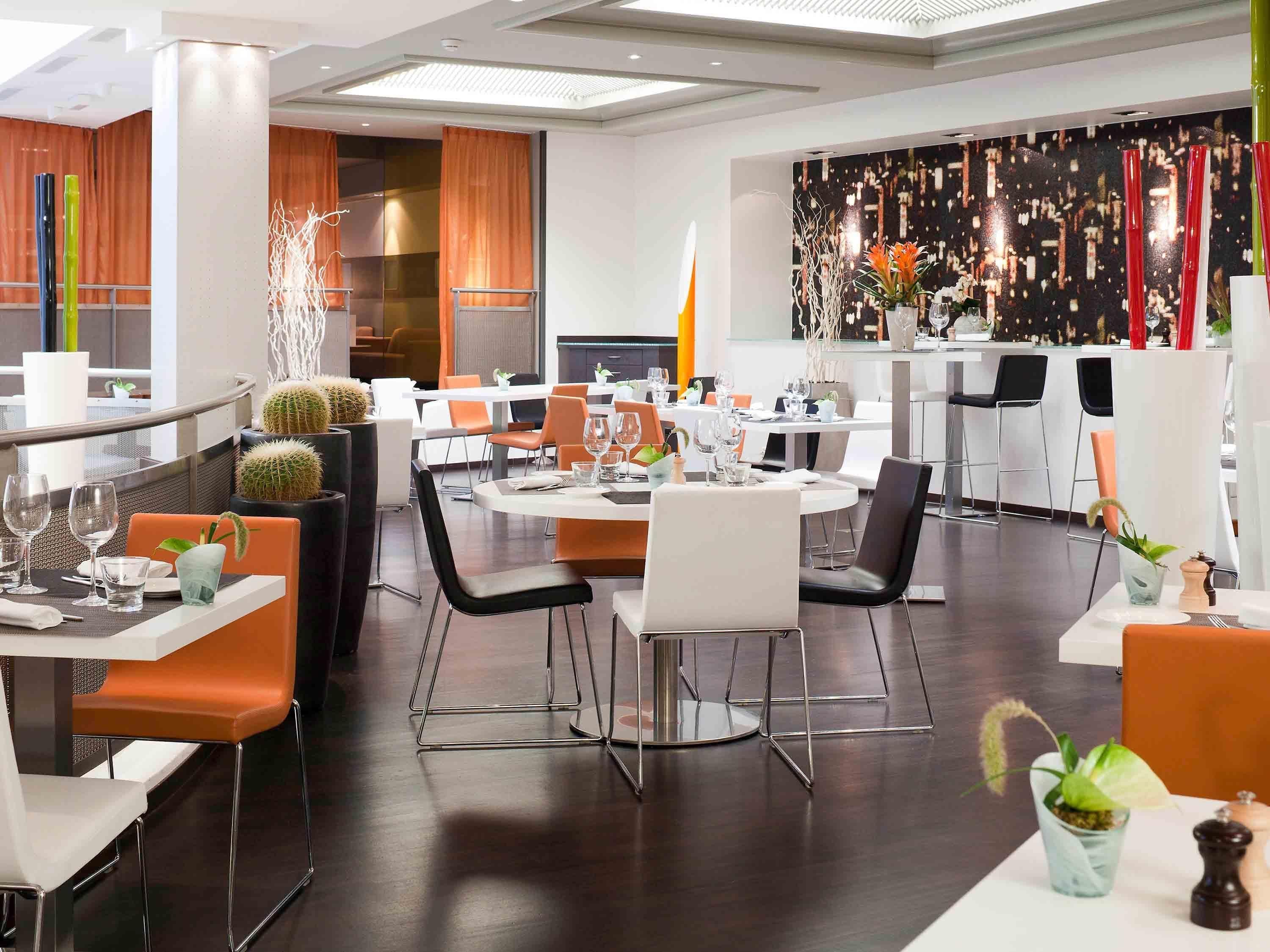 A modern restaurant with round tables, orange chairs, and a black and white color scheme.