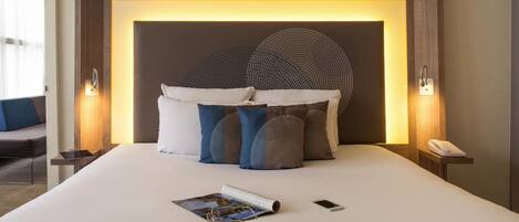 Une chambre d’hôtel avec un grand lit, une tête de lit au motif circulaire, des lampes de chevet, un téléphone et un magazine.
