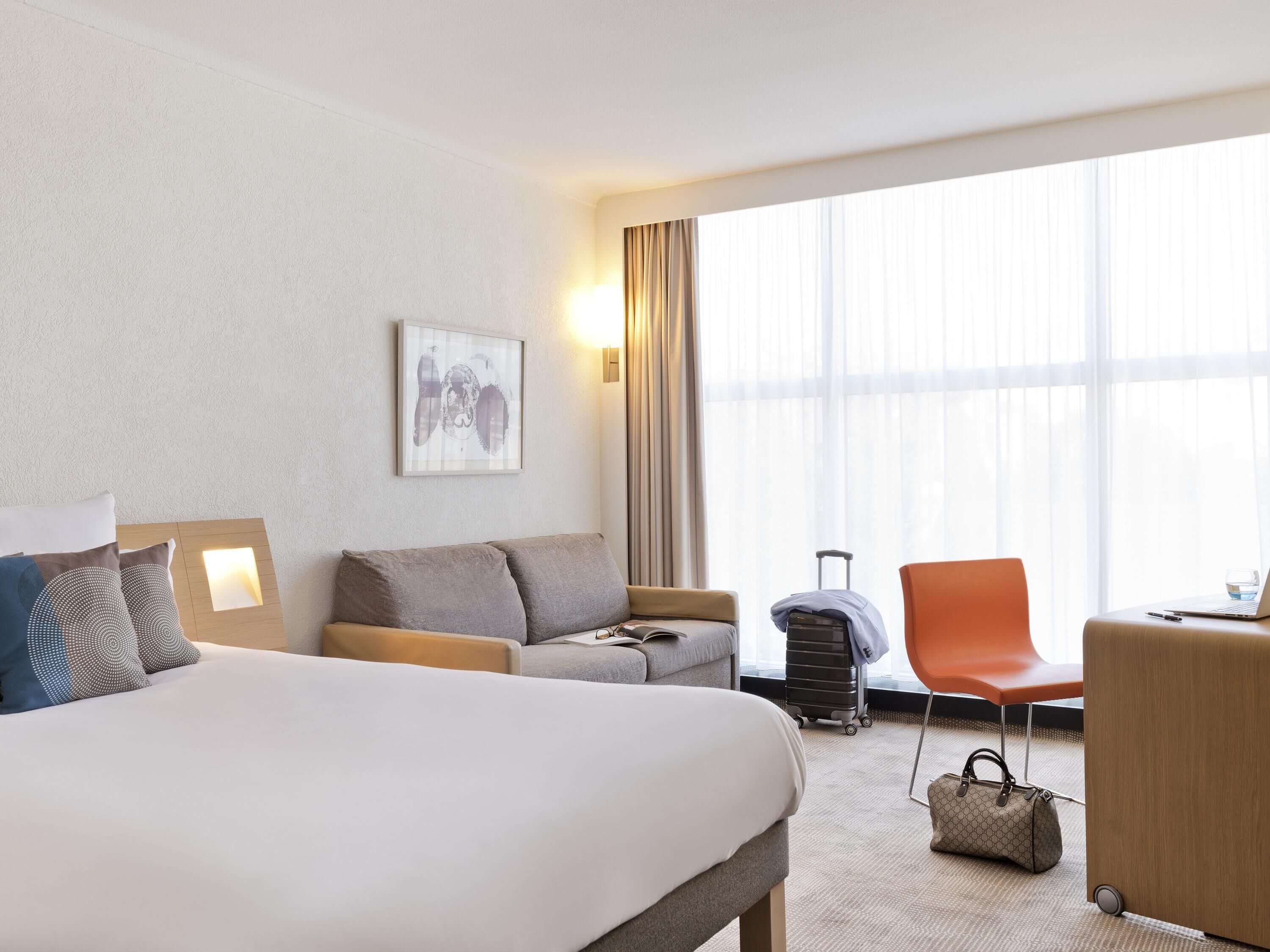 Ett hotellrum med en säng, en soffa, ett skrivbord, en stol, en resväska och en handväska.