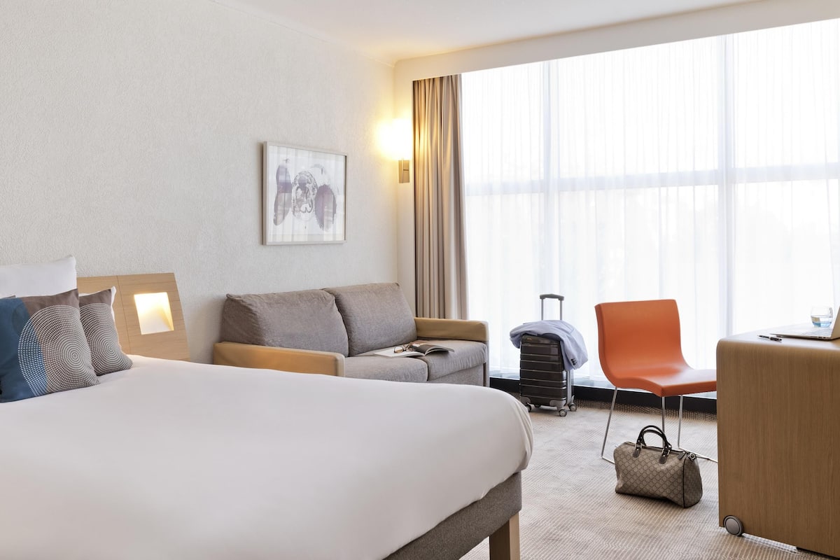 Ett hotellrum med en säng, en soffa, ett skrivbord, en stol, en resväska och en handväska.
