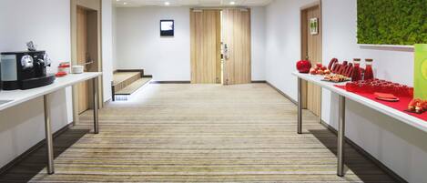 A hotel corridor with a carpeted floor, a coffee machine, and a buffet table with food and drinks.