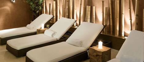 A spa room with three reclining chairs, each with a small wooden side table and a lit candle.