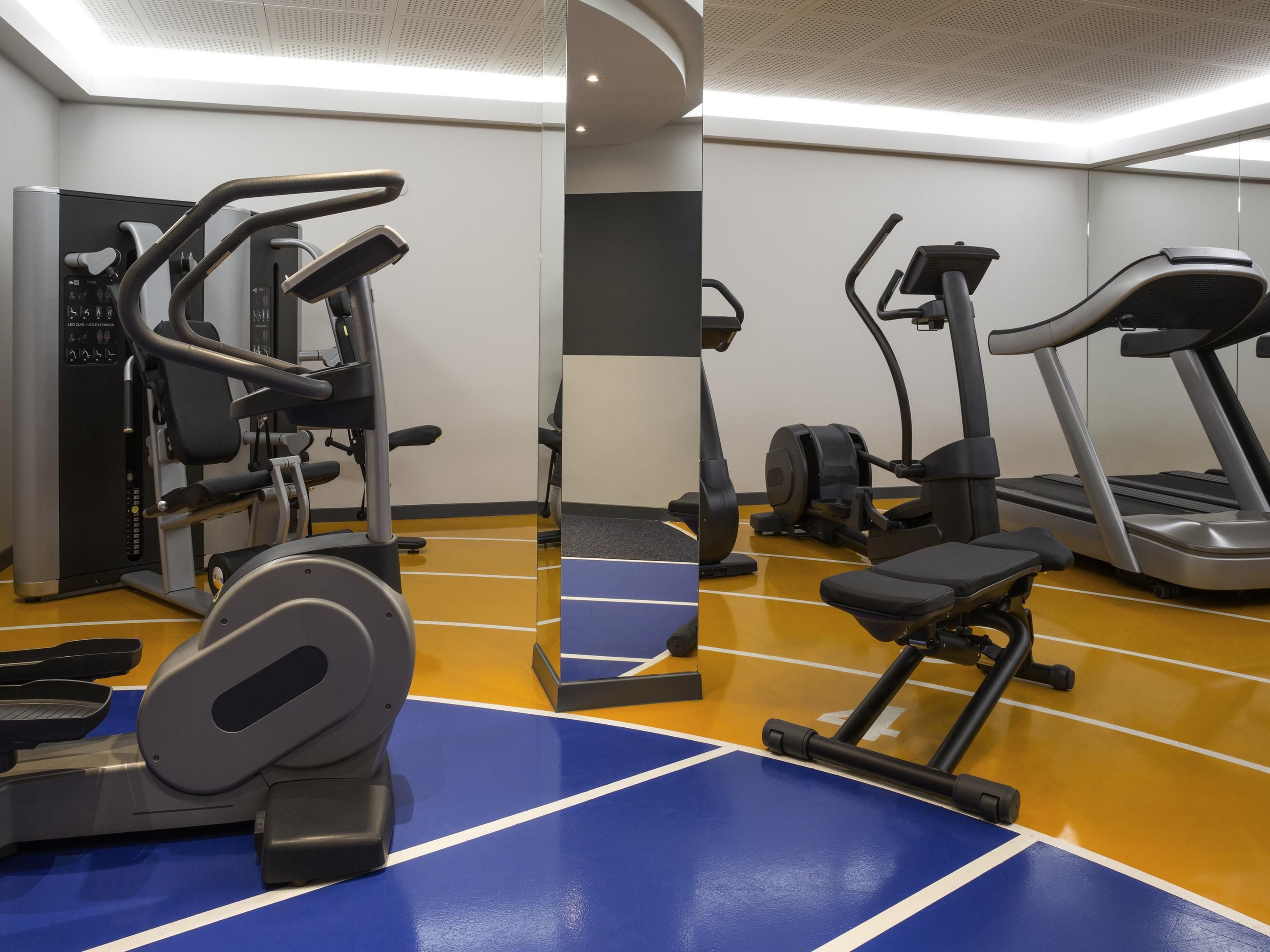 A gym with cardio machines, weight equipment, and a blue and yellow floor.
