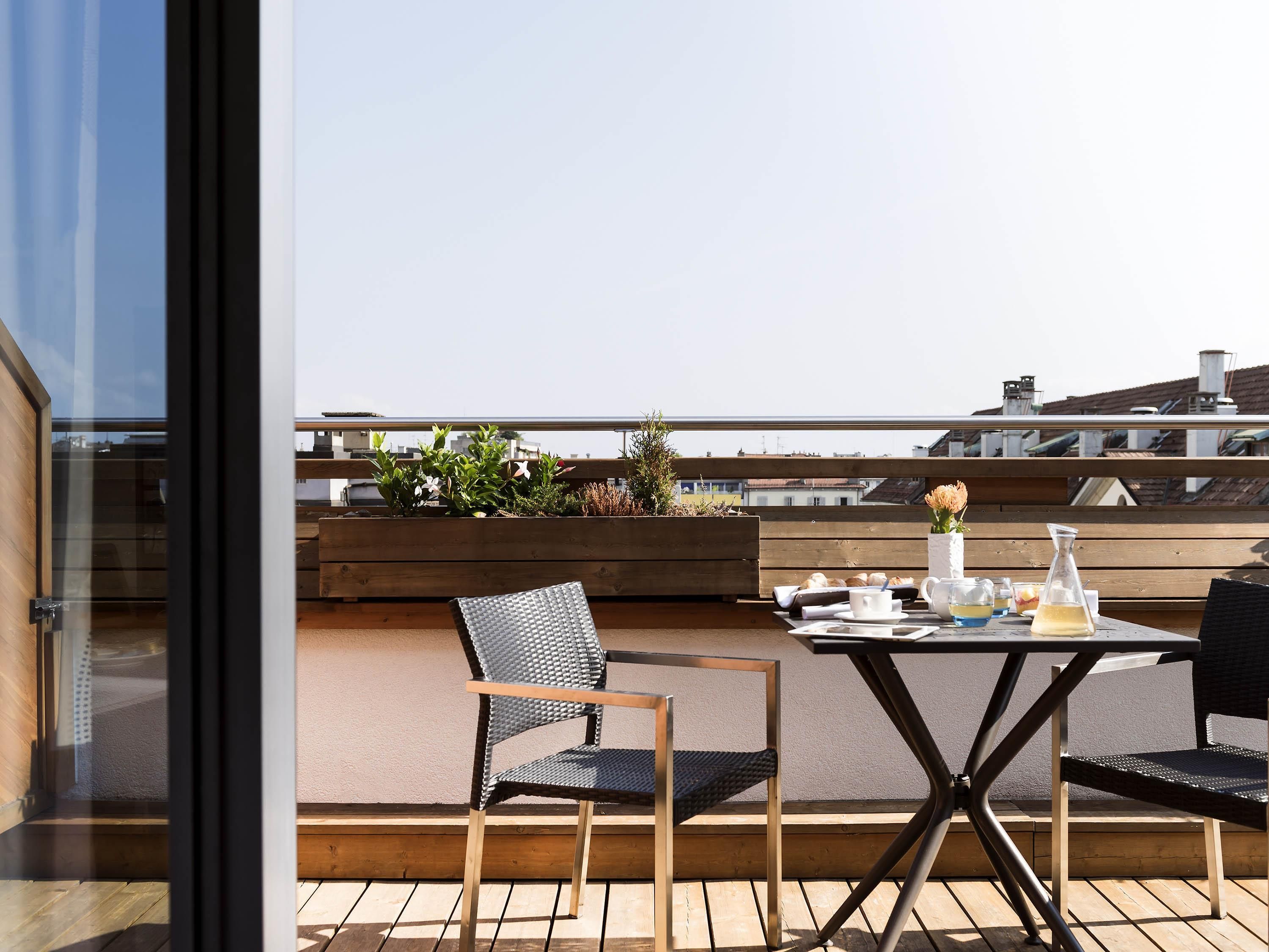 A rooftop terrace with a table set for two, two chairs, and a wooden planter with plants.