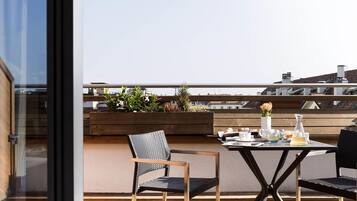 A rooftop terrace with a table set for two, two chairs, and a wooden planter with plants.
