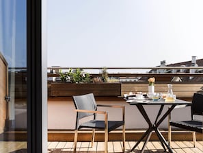A rooftop terrace with a table set for two, two chairs, and a wooden planter with plants. - Novotel Geneve Centre (Geneva)