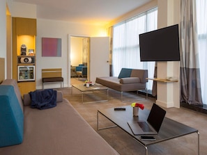 Una habitación de hotel moderna con sofá, mesa de centro, televisor y minibar.