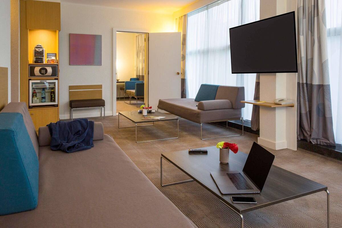 Moderni hotellihuone, jossa on sohva, sohvapöytä, televisio ja minibaari.