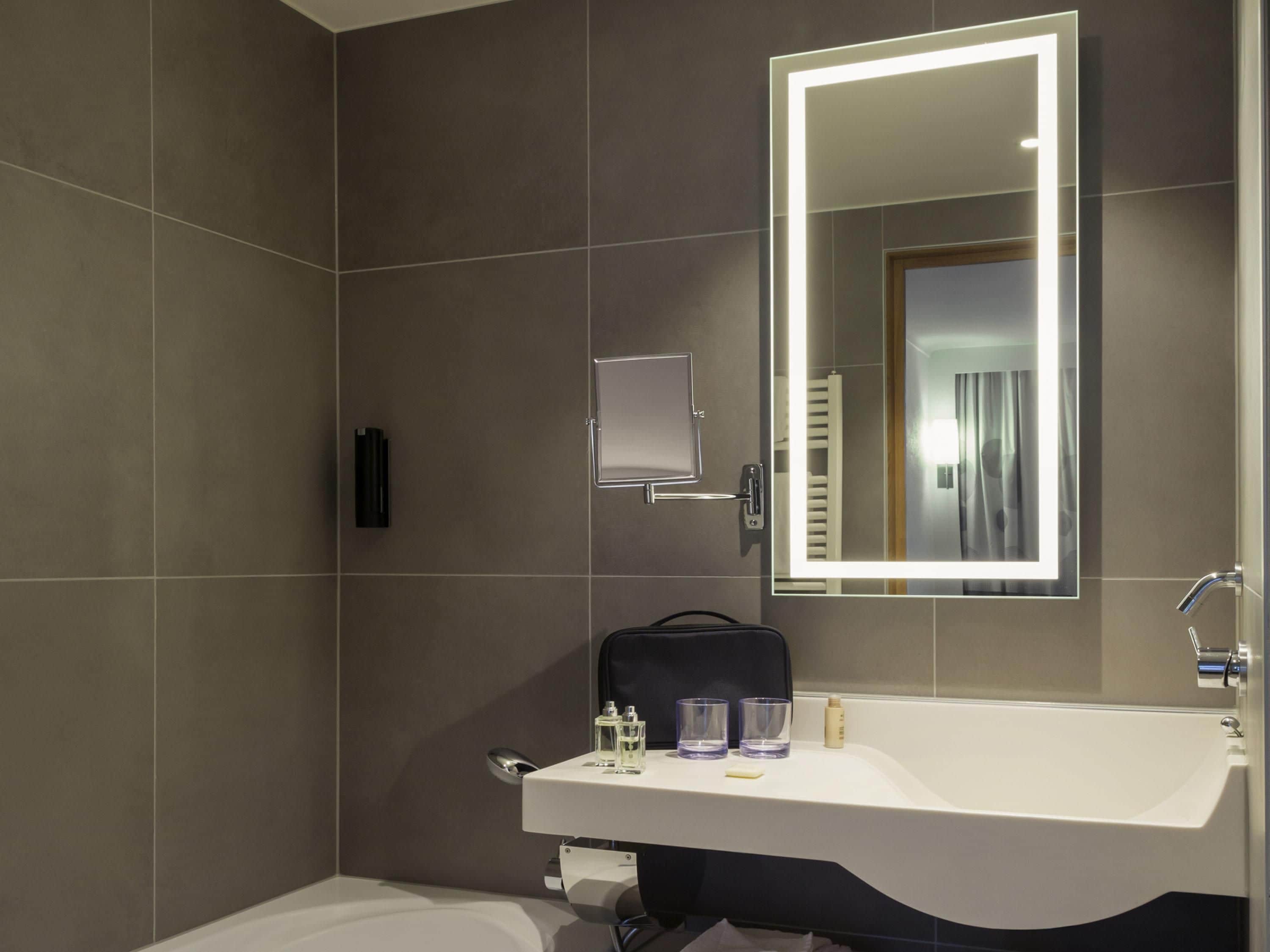 A modern bathroom with a large mirror, a sink, and a towel rack.