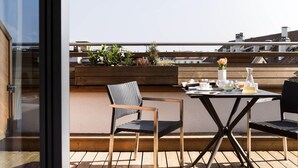 A rooftop terrace with a table set for two, two chairs, and a wooden planter with plants. - Novotel Geneve Centre (Geneva)
