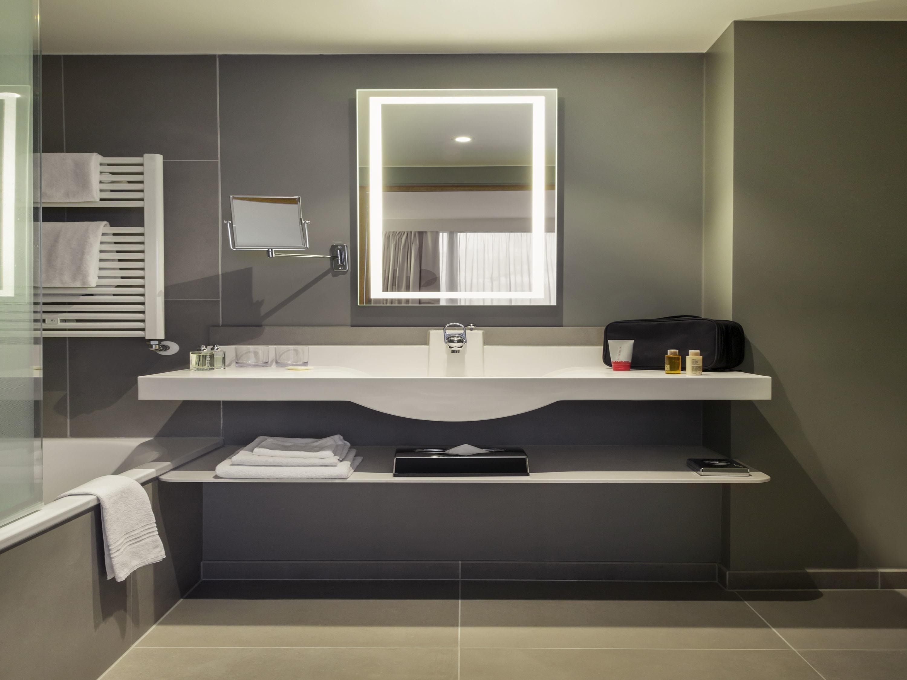 A modern bathroom with a vanity, a mirror, a towel rack, and a shelf with toiletries.