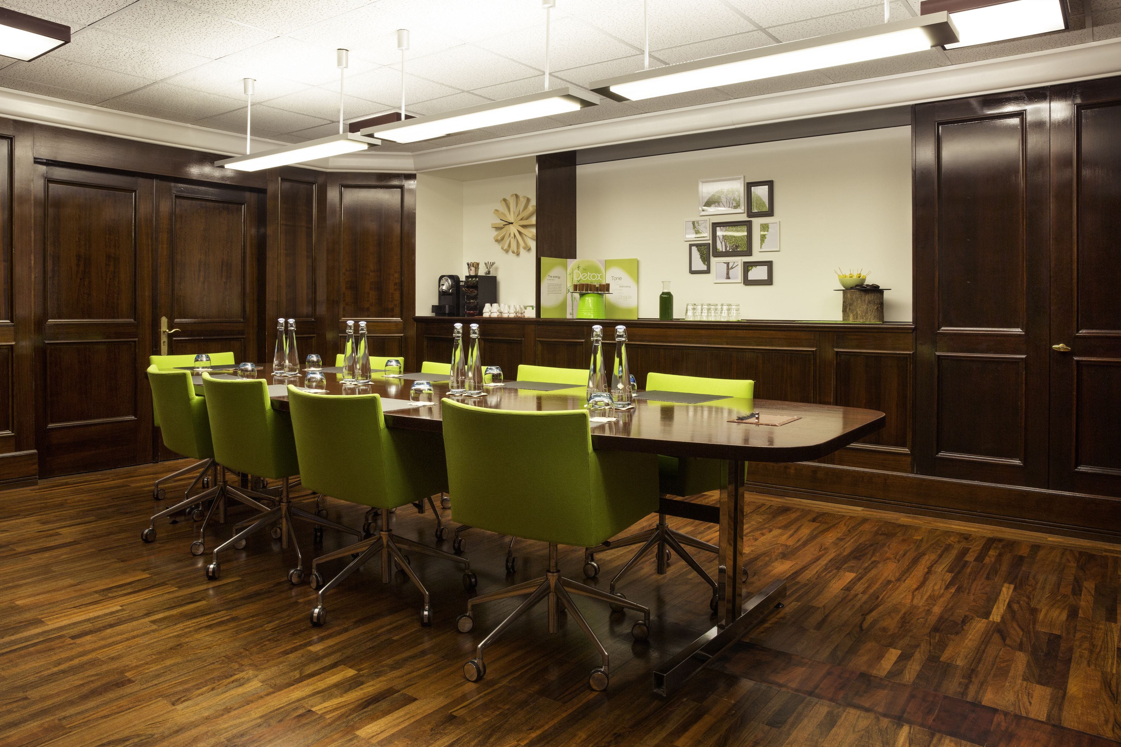 A conference room with a long table, green chairs, and wooden paneling.